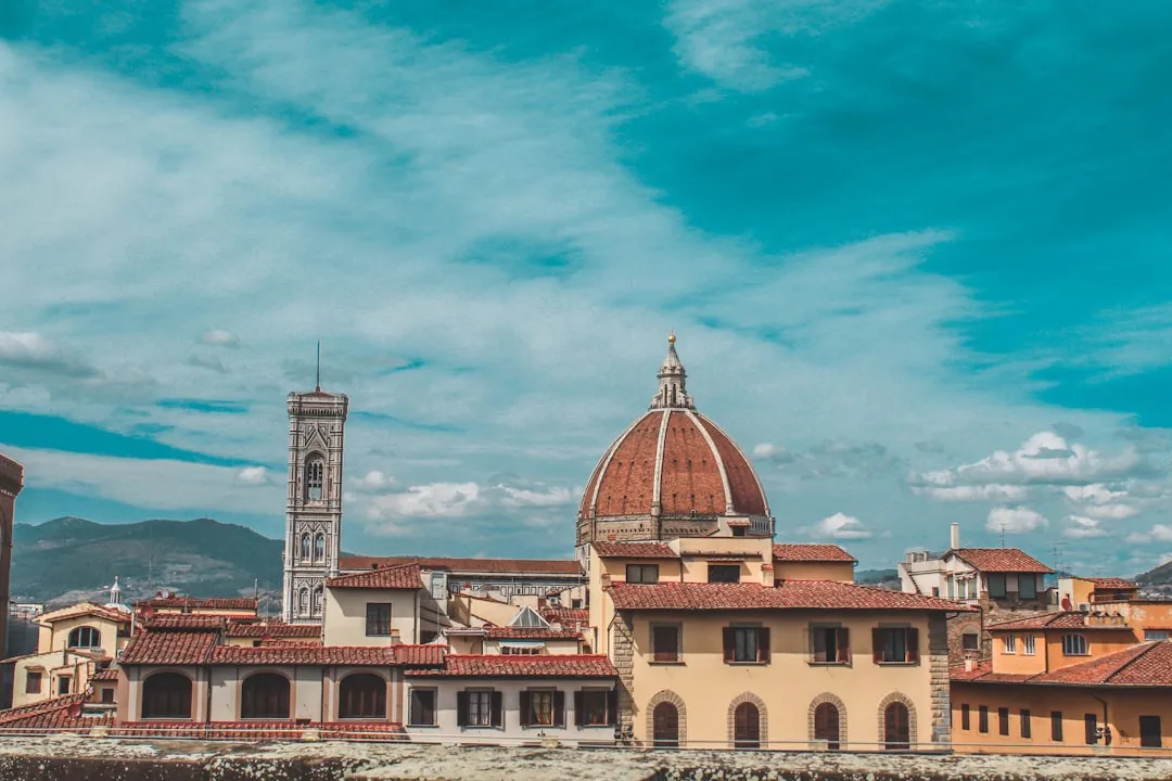 A scenic view of Florence, Italy, featuring the iconic dome of the Florence Cathedral and surrounding historic buildings under a cloudy sky.