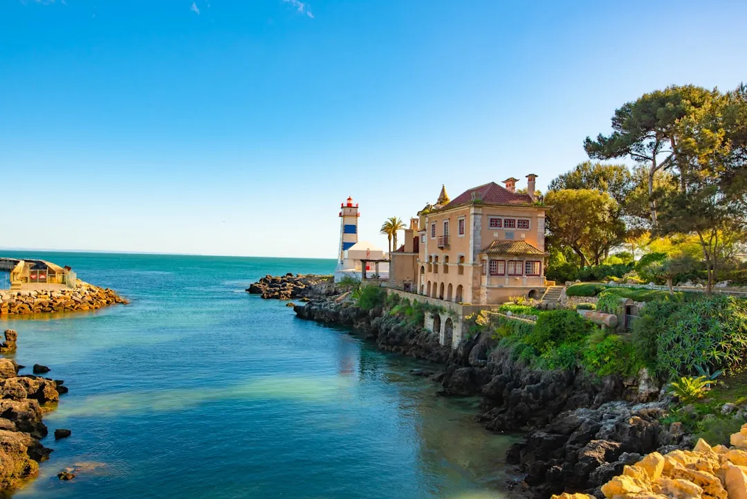 Coastal lighthouse and villa perched on rocky Mediterranean shore with turquoise waters