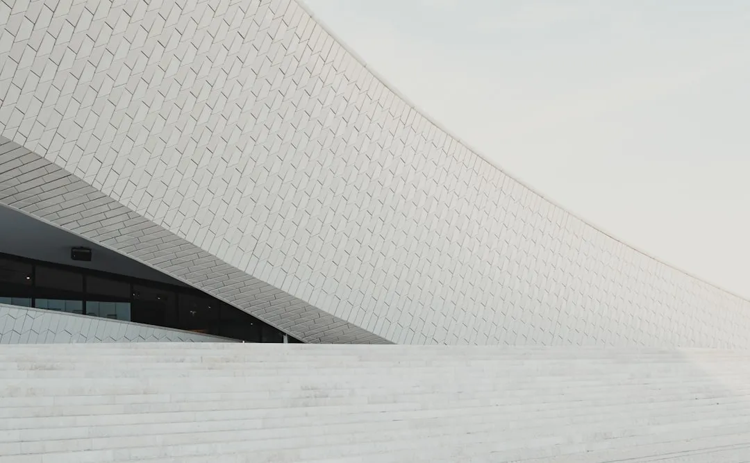 Minimalist white building facade with geometric pattern design and curved structure against light background